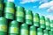 Group of green stacked biofuel drums against blue sky with cloud