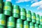 Group of green stacked biofuel drums against blue sky with cloud