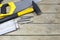 Group Of Hand Tools- Black Yellow Hammer, Saw, Folding Ruler And Nails On Wooden Table