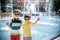 Group of happy children playing outdoors near pool or fountain. Kids embrace show thumb up in park during summer vacation. Dressed