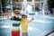 Group of happy children playing outdoors near pool or fountain. Kids embrace show thumb up in park during summer vacation. Dressed