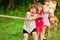 Group of happy children playing tug of war outside on grass. Kids pulling rope at park. Summer camp