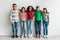 Group of happy diverse preteen children embracing over gray background