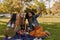 Group of happy diverse three female friends sitting together on blanket over the green grass enjoying at picnic taking