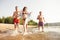 Group of happy friends running in to water - active people having fun on the beach on vacation