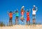 Group of happy little kids jump on sand dune up