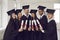 Group of happy multiethnic university graduates in black mantles standing with diplomas in hands