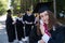 Group of happy students in graduation gowns outdoors. A young girl boasts of her diploma.