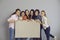 Group of happy young women standing together, smiling and showing blank mockup banner