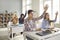 Group of high school or college students raising hands sitting at desks in classroom