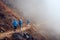 Group Hikers with Backpacks walking down on Mountain Trail in foggy mountains