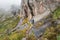 Group of hikers hikers, with hiking guide in front walk near tall rocky cliffs, grass around, typical landscape seen during trek