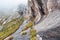 Group of hikers, with hiking guide in front walk near tall rocky cliffs, grass around, typical landscape seen during trek to Pic