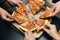 Group of hungry friends sitting at desk and sharing delicious lunch on table background. Male hands taking slices of