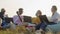 Group of international friends sitting in nature with laptops in cushioned chairs and chatting, front view. Four