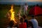 Group of kids listening instructor, while sitting around campfire at twilight.