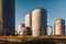 a group of large metal tanks sitting in a field next to a dirt road and a blue sky with clouds