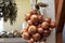 A group of large onion heads with brown husks hangs on a shop window in a store.