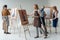 group of male and female adult students in aprons painting together on easels