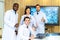 Group of medical practitioners in lab coats gesturing thumbs up while sitting and standing with smiling on camera. Four colleagues