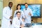 Group of medical practitioners in lab coats gesturing thumbs up while sitting and standing with smiling on camera. Four colleagues