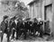 Group of men with guns and top hats breaking into a barn