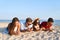 Group of millenials using smartphones laying together on beach towel near sea on summer sunset. Young people addicted by
