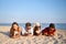 Group of millenials using smartphones laying together on beach towel near sea on summer sunset. Young people addicted by