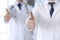 Group of modern doctors standing as a team with thumbs up or Ok sign in hospital office, close-up. Physicians ready to examine and