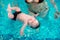 A group of mothers with their young children in a children`s swimming class with a coach.