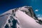 Group of mountain climbers climb the slope to the peak in sunny weather with sledges and tents equipment for overnight stays.