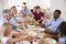 Group Of Multi-Generation Family And Friends Sitting Around Table And Enjoying Meal