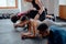 Group of multiracial young adults doing plank exercises with trainer assisting at the gym