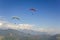 A group of paragliders on colored parachutes in a clear blue sky over a mountain valley