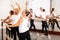 Group of people doing exercises using barre in gym with focus to fit athletic toned woman in foreground in health