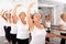 Group of people doing exercises using barre in gym with focus to fit athletic toned woman in foreground in health