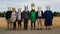 Group of people with masks in a row standing in a field.