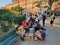 Group of people playing chess in a park under a beautiful sun and the amused looks of tourists.