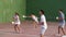 Group of people playing friendly pelota goma match on outdoor summer court with fronton wall, swinging wooden paleta to