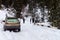 A group of people push out a car stuck on a snow-covered forest road