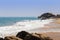 Group of people swimming on a large sandy beach with big rocks