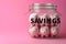 Group of pink piggy banks in a glass jar on pink. Personal savings and financial investment, money storage, money boxes. Finance
