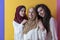 Group portrait of beautiful Muslim women two of them in a fashionable dress with hijab isolated on a yellow background