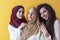 Group portrait of beautiful Muslim women two of them in a fashionable dress with hijab isolated on a yellow background