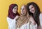 Group portrait of beautiful Muslim women two of them in a fashionable dress with hijab isolated on a yellow background