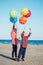 Group portrait of two funny white Caucasian children kids with colorful bunch of balloons, playing running on beach on sunset