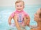 Group portrait of white Caucasian mother and baby daughter playing in water diving in swimming pool inside, looking in camera