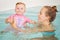 Group portrait of white Caucasian mother and baby daughter playing in water diving in swimming pool inside, looking in camera