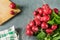 Group of red fresh radishes on gray background with wooden board and dishtowel.