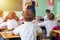 group of school kids sitting and listening to teacher in classroom from back